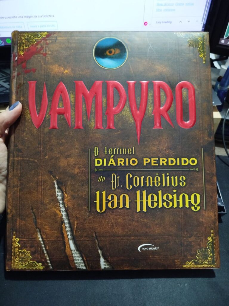 Capa do livro “Vampyro: O Terrível Diário Perdido do Dr. Cornélius Van Helsing”, edição da Novo Século. A capa tem fundo marrom envelhecido, detalhes ornamentais dourados, um olho amarelo em uma pequena janela circular e o título em letras grandes vermelhas.