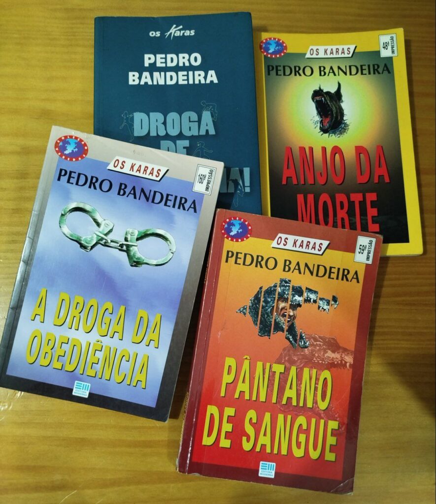 Quatro livros da série “Os Karas”, de Pedro Bandeira — “A Droga da Obediência”, “Pântano de Sangue”, “Anjo da Morte” e “Droga de Americana!” — dispostos sobre uma mesa de madeira.